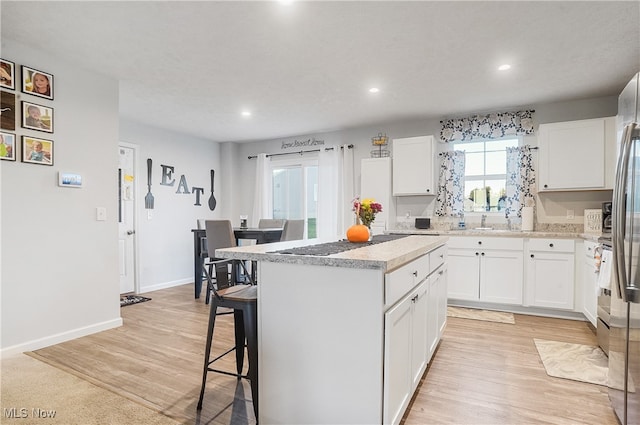 kitchen featuring a breakfast bar area, a kitchen island, white cabinetry, and light wood-type flooring