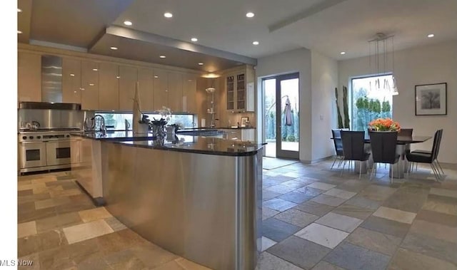 kitchen featuring a healthy amount of sunlight, decorative light fixtures, exhaust hood, and an island with sink