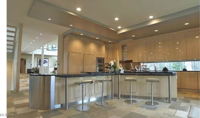 kitchen with dark stone countertops, built in appliances, plenty of natural light, and a breakfast bar area