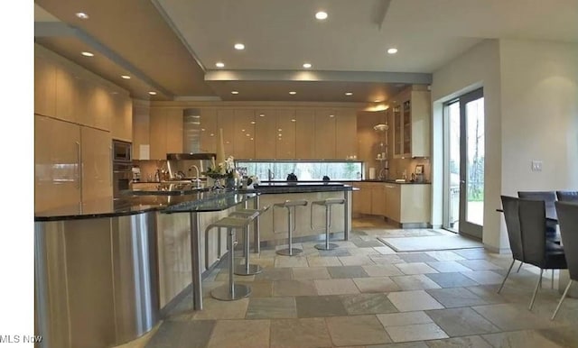 kitchen with kitchen peninsula, decorative backsplash, appliances with stainless steel finishes, a kitchen bar, and dark stone countertops