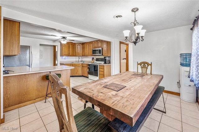 tiled dining room featuring a textured ceiling, sink, and ceiling fan with notable chandelier