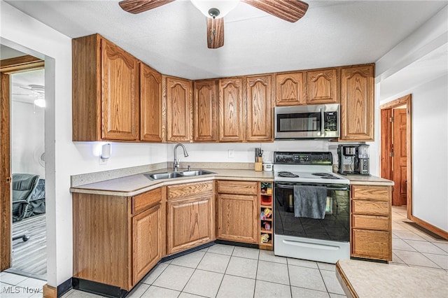 kitchen with electric range, ceiling fan, light tile patterned floors, a textured ceiling, and sink