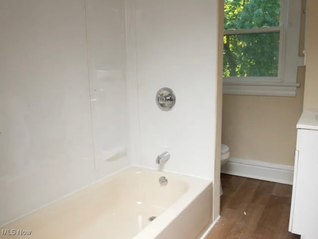 full bathroom with toilet, hardwood / wood-style floors, vanity, and washtub / shower combination