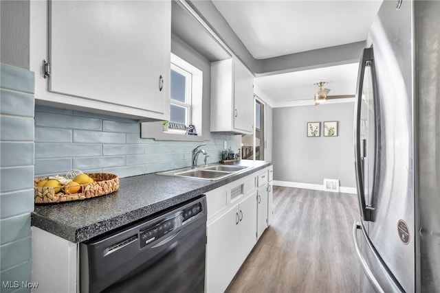 kitchen with black dishwasher, sink, light hardwood / wood-style floors, white cabinets, and stainless steel refrigerator