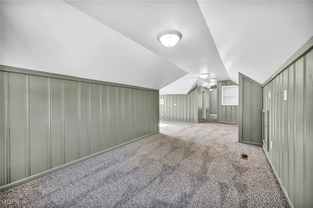 bonus room featuring carpet flooring, vaulted ceiling, and wooden walls