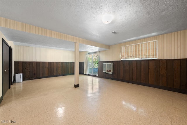 basement with wooden walls, a textured ceiling, and heating unit