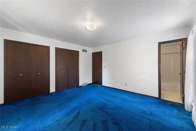 unfurnished bedroom featuring ensuite bath, multiple closets, and dark carpet