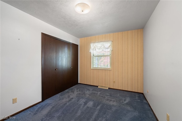 unfurnished bedroom with a closet, wood walls, a textured ceiling, and dark carpet