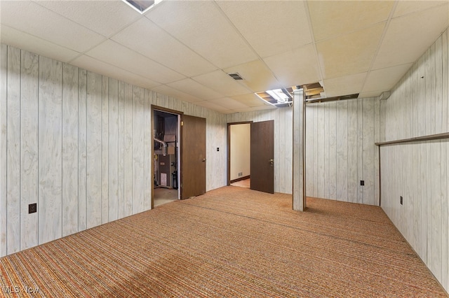 basement with wooden walls, a drop ceiling, and light carpet