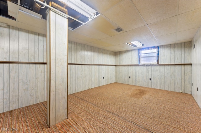 basement featuring a paneled ceiling, wood walls, and carpet floors