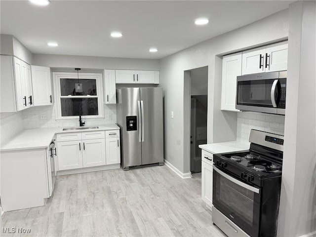 kitchen featuring tasteful backsplash, stainless steel appliances, sink, light hardwood / wood-style floors, and white cabinetry