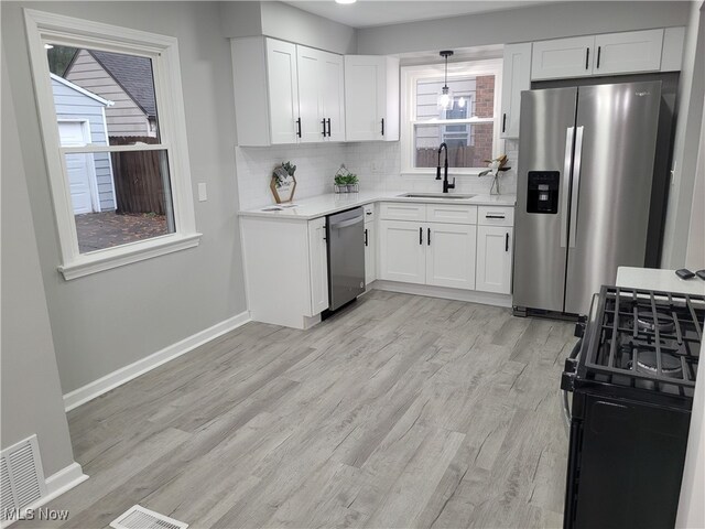 kitchen with sink, hanging light fixtures, light hardwood / wood-style flooring, white cabinets, and appliances with stainless steel finishes