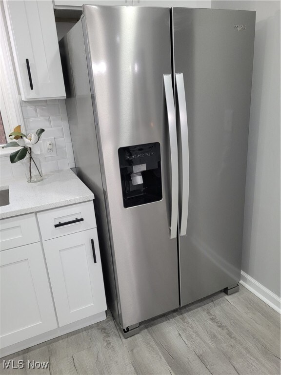 kitchen with white cabinets, stainless steel fridge with ice dispenser, light wood-type flooring, and light stone counters