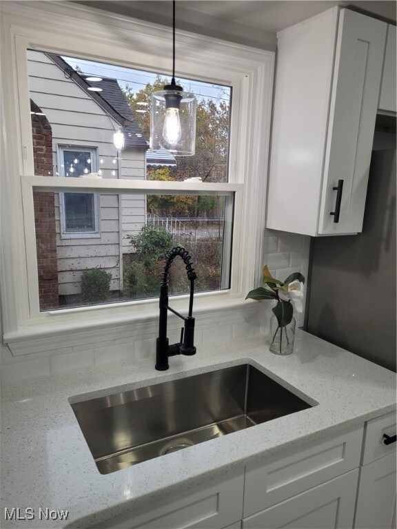 interior details featuring white cabinets, light stone countertops, sink, and hanging light fixtures