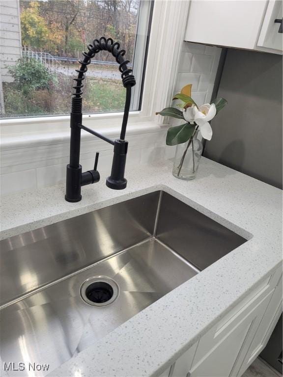 room details featuring light stone counters, white cabinetry, and sink