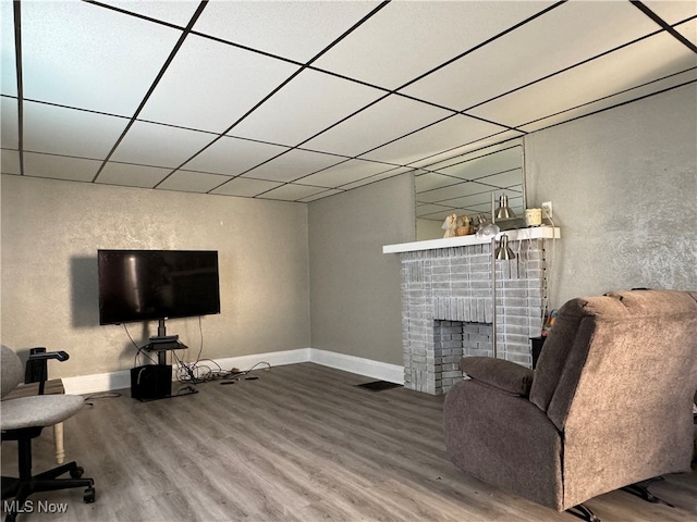 living room featuring a drop ceiling, a brick fireplace, and hardwood / wood-style flooring