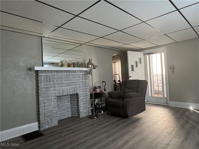 living room with hardwood / wood-style floors, a paneled ceiling, and a brick fireplace