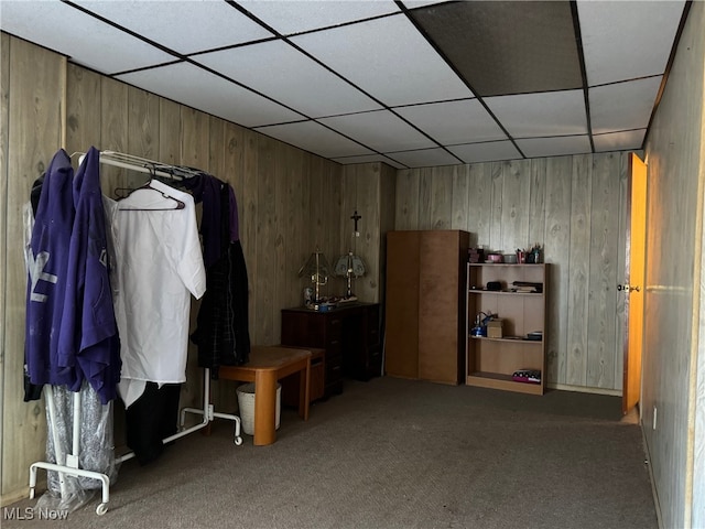 interior space featuring a paneled ceiling, carpet flooring, and wooden walls