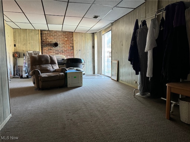 carpeted living room featuring a drop ceiling and wooden walls