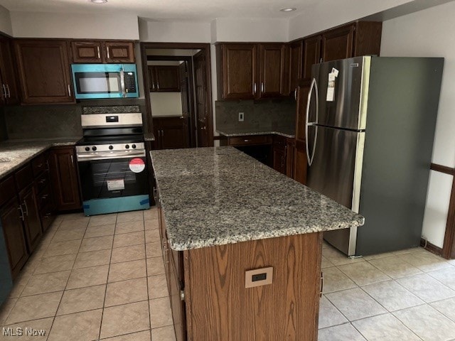 kitchen with dark stone countertops, light tile patterned floors, appliances with stainless steel finishes, tasteful backsplash, and a kitchen island