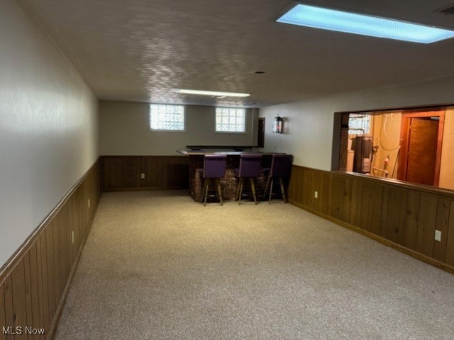 basement featuring light colored carpet, wooden walls, and bar area