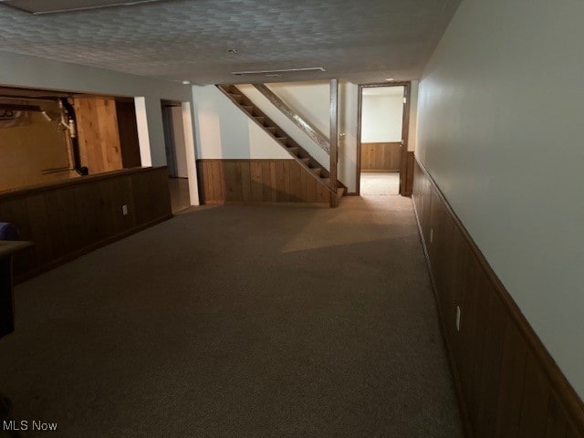 basement featuring a textured ceiling, wood walls, and light carpet