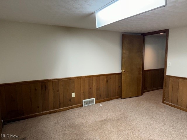 unfurnished room with a textured ceiling, wood walls, and light carpet