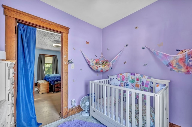 bedroom featuring light hardwood / wood-style flooring, a nursery area, and a textured ceiling