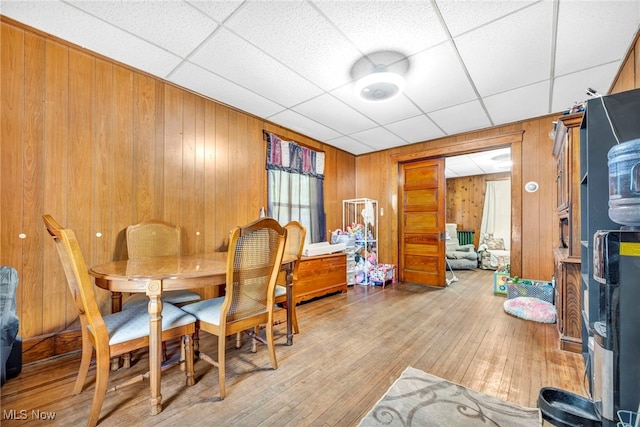 dining space featuring light hardwood / wood-style flooring, a paneled ceiling, and wooden walls