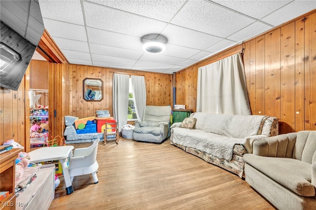 living room with light hardwood / wood-style floors, wood walls, and a drop ceiling