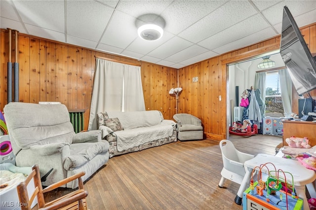 living room featuring a paneled ceiling, hardwood / wood-style flooring, and wooden walls