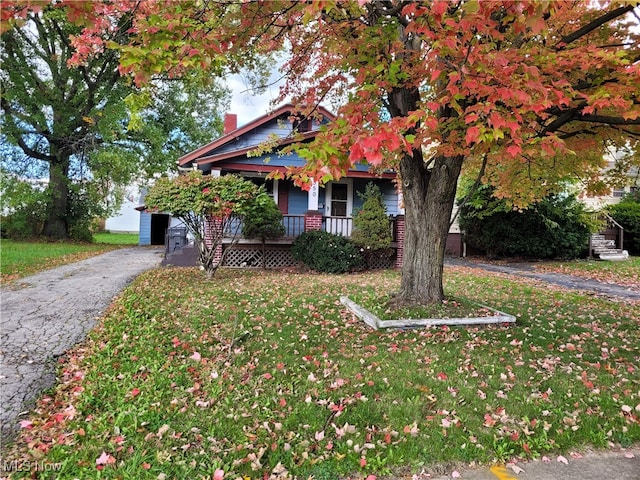 view of property hidden behind natural elements with covered porch and a front yard