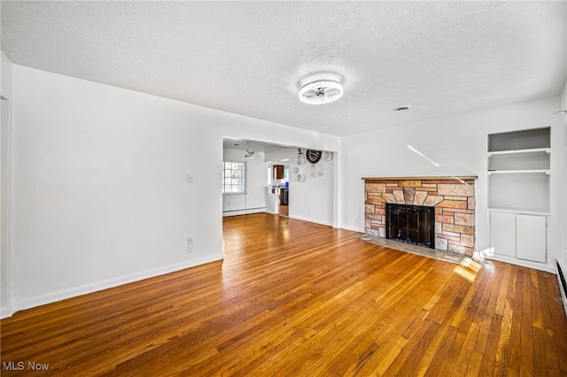 unfurnished living room featuring a textured ceiling, wood-type flooring, a fireplace, built in shelves, and baseboard heating