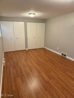 unfurnished bedroom with multiple closets, a textured ceiling, and hardwood / wood-style floors