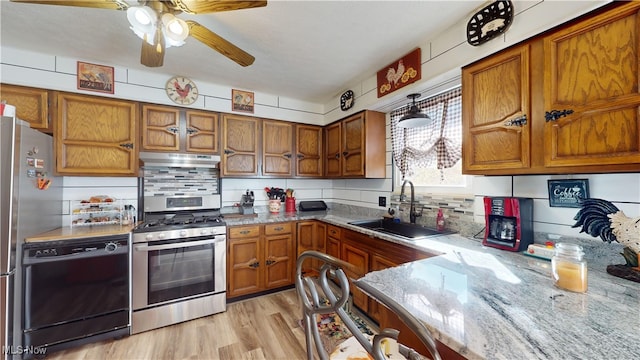 kitchen with appliances with stainless steel finishes, sink, light wood-type flooring, light stone counters, and decorative backsplash