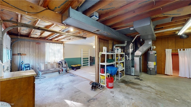 basement featuring water heater, heating unit, and wooden walls