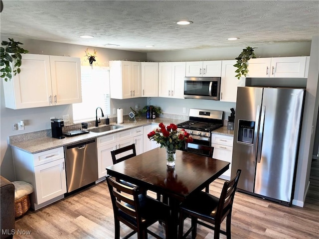 kitchen featuring white cabinetry, sink, light hardwood / wood-style floors, a textured ceiling, and appliances with stainless steel finishes