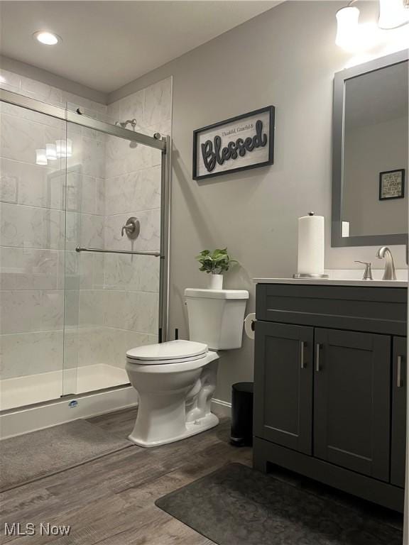 bathroom featuring wood-type flooring, vanity, toilet, and a shower with shower door