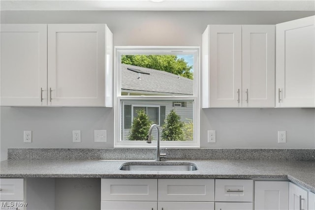 kitchen featuring light stone countertops, white cabinetry, and sink