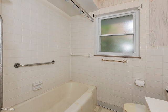 full bathroom featuring tiled shower / bath, vanity, toilet, and tile walls