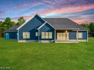 back house at dusk with a patio and a lawn