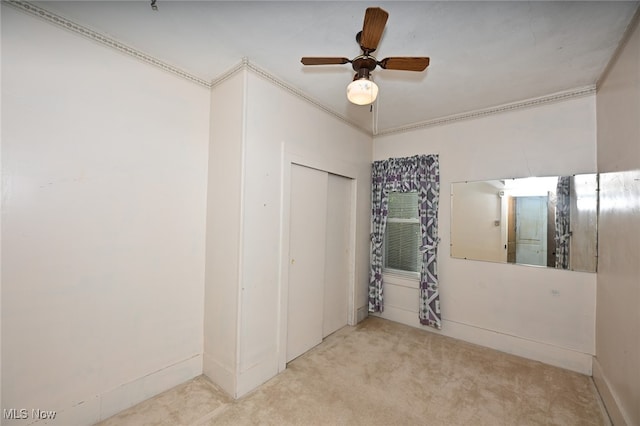 unfurnished bedroom with a closet, ceiling fan, ornamental molding, and light colored carpet