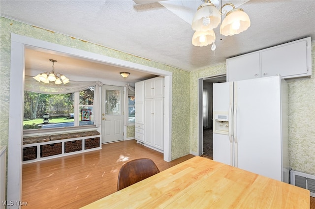 kitchen with white fridge with ice dispenser, hardwood / wood-style floors, decorative light fixtures, an inviting chandelier, and white cabinetry