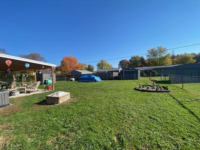 view of yard featuring a storage shed, cooling unit, and a fire pit