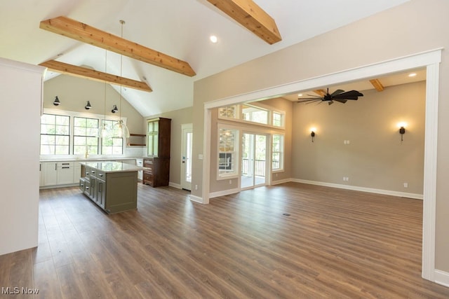 unfurnished living room with beam ceiling, ceiling fan, a healthy amount of sunlight, and dark hardwood / wood-style floors