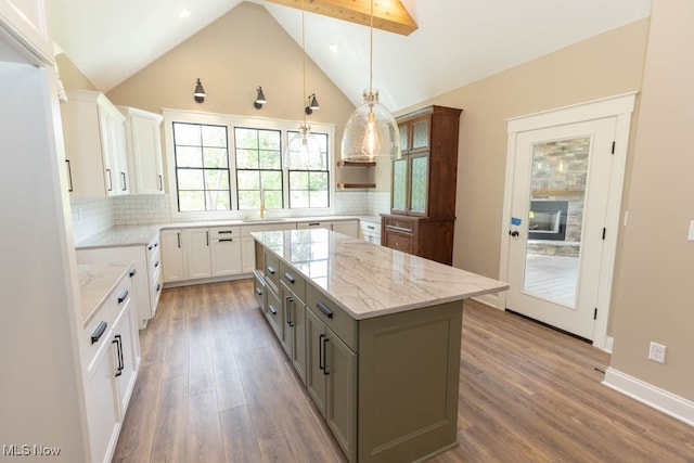 kitchen featuring a kitchen island, light stone counters, hardwood / wood-style floors, decorative backsplash, and white cabinets