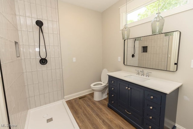 bathroom with hardwood / wood-style floors, vanity, toilet, and a tile shower