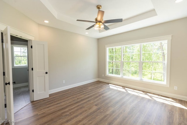 spare room featuring ceiling fan, dark wood-type flooring, a wealth of natural light, and a tray ceiling