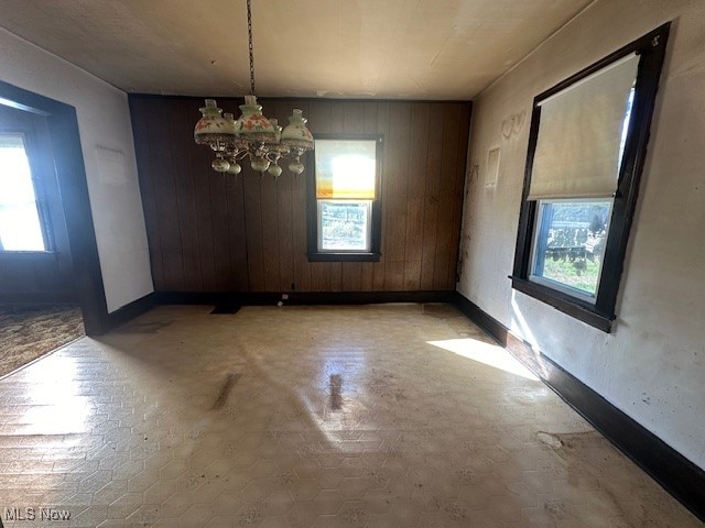 unfurnished dining area with concrete floors, wood walls, a chandelier, and plenty of natural light