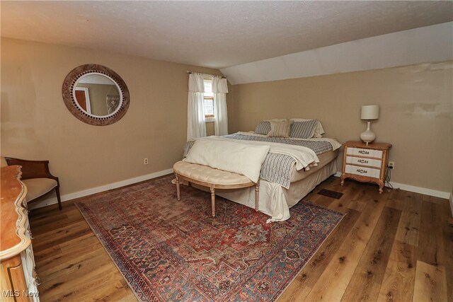 bedroom with a textured ceiling, lofted ceiling, and hardwood / wood-style floors